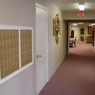 A hallway with mailboxes on the wall, leading to a room with tables and chairs.