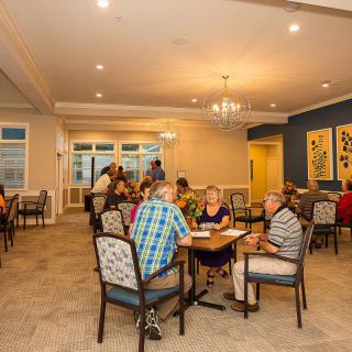 A group of seniors socializing in a dining area, with several tables and chairs arranged for comfort and conversation.