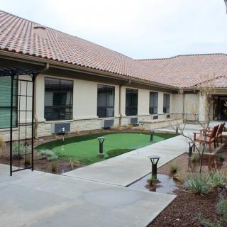 A courtyard with a pathway, outdoor seating, and landscaped greenery surrounded by a building with multiple windows.