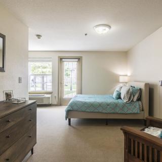 A spacious and well-lit bedroom featuring a comfortable bed, dresser, and large windows.