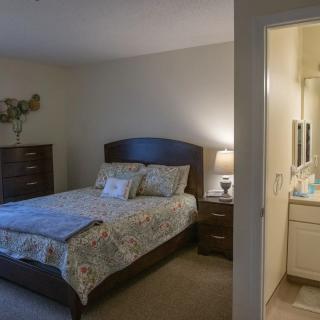 A cozy bedroom interior featuring a neatly made bed, nightstand with a lamp, and an open door leading to a bathroom.
