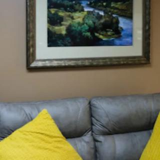 A cozy living room setup with a gray couch, yellow pillows, and landscape artwork hanging on the wall.