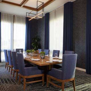 A modern and elegant dining or conference room featuring a large wooden table surrounded by upholstered chairs, with soft lighting and stylish curtains.