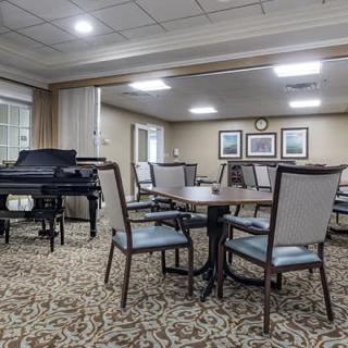 A cozy, carpeted room with a grand piano and several tables and chairs arranged for seating.