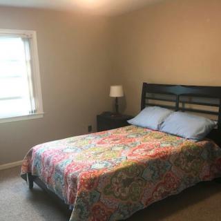 A cozy bedroom featuring a bed with colorful bedding, a bedside lamp, and a window allowing natural light.