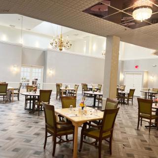 A spacious and elegantly designed dining area with several tables and chairs, lit by chandeliers.