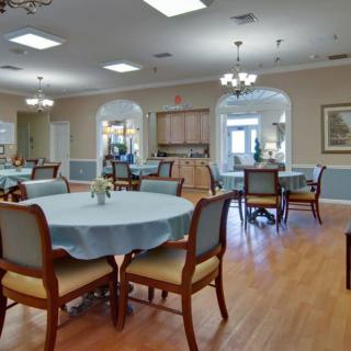 A spacious dining area with neatly arranged tables and chairs, featuring a wooden floor and elegant chandeliers.