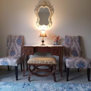 A charming vanity setup featuring a decorative mirror, elegant chairs, and a soft lamp, creating a cozy corner.