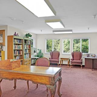 A spacious office with a wooden desk, bookshelves, and comfortable seating by large windows.