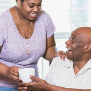 A happy moment of care and connection as a person hands a cup to an elderly man.