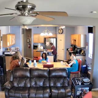 A cozy indoor gathering with people engaged in various activities around a dining table and kitchen.