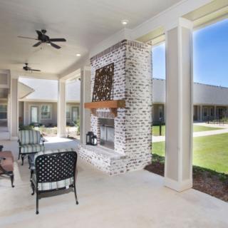A spacious covered patio with a brick fireplace, ceiling fans, and outdoor furniture overlooking a garden.