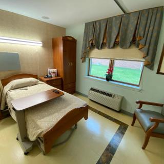 A hospital room with a single bed, wooden furniture, and a window with drapes.