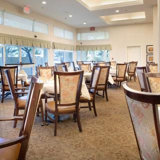 A spacious, elegantly furnished dining area with multiple tables and chairs, featuring large windows that allow natural light to brighten the room.