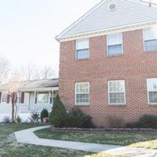 A suburban brick house with a front yard and pathway leading to the entrance.