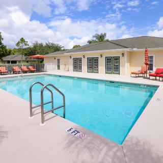 An outdoor swimming pool with poolside chairs and a residential building in the background on a sunny day.