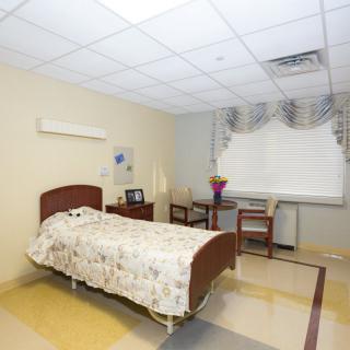 A clean and simple hospital room with a single bed and chairs by the window.