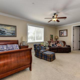 A spacious bedroom featuring a bed, sofa, ceiling fan, and wall artwork.