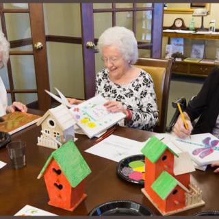 A group of elderly individuals engaged in painting colorful birdhouses together at a table.