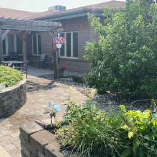 A cozy outdoor patio area with lush greenery and brick pathways.