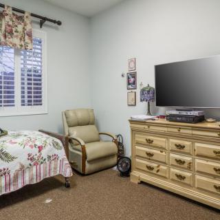A cozy bedroom with a bed, dresser, television, and armchair.