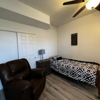 A cozy bedroom featuring a single bed with a patterned blanket, a comfy chair, and modern furnishings.