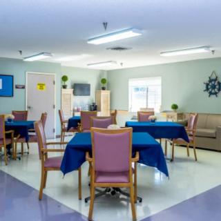 A well-lit community dining area with tables covered in blue tablecloths and surrounded by cushioned chairs.