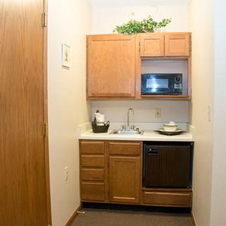 A compact kitchenette with wooden cabinets, a microwave, and a sink.