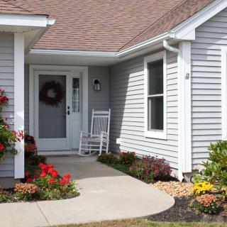 A welcoming front porch of a house with a rocking chair, flowers, and a wreath on the door.