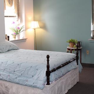 A cozy bedroom with a neatly made bed, a floor lamp, and a small plant by the window.