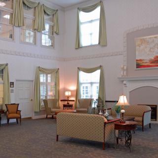 A spacious and elegantly decorated living room features high ceilings, large windows with draped curtains, and comfortable seating around a coffee table.
