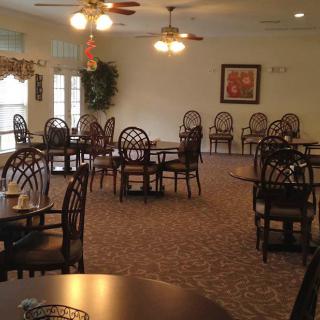 An empty dining room with neatly arranged chairs and tables, featuring overhead lighting and carpeted flooring.