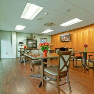 A modern dining area with wooden flooring, tables, and chairs adorned with flower arrangements.