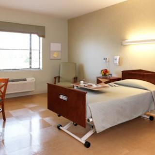 A well-lit patient room in a hospital, featuring a bed, chair, and window.