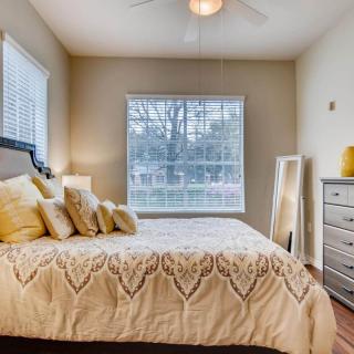 A cozy and stylish bedroom with a large window, featuring a bed adorned with decorative pillows and a neatly arranged dresser.