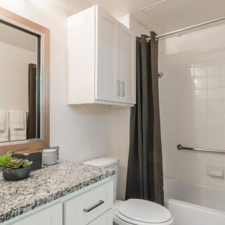 A modern bathroom featuring a granite countertop and white cabinetry, with a dark shower curtain complementing the clean design.