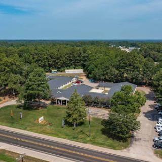 Aerial view of a commercial building surrounded by trees and a roadway.