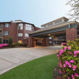 A residential building with a landscaped entrance featuring blooming flowers and a driveway.
