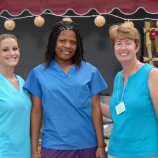 A group of three women smiling outdoors in casual attire.