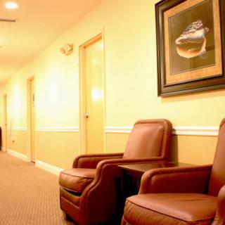 A well-lit indoor hallway featuring two leather chairs and a framed artwork on the wall.
