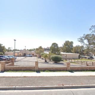 A view of a parking lot with trees and buildings under a clear blue sky.