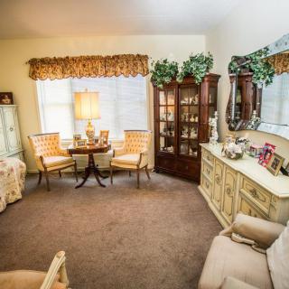 A traditional living room with classic furniture, including a wooden cabinet, chairs, and a small table beside a lamp.