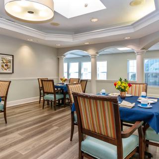 A well-lit dining area with several tables and chairs arranged, featuring elegant decor and large windows.