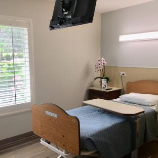 A well-lit hospital patient room featuring a bed, bedside table, and a wall-mounted TV.
