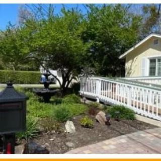A well-maintained garden with a tree and pathway leading to a house with a white fence.