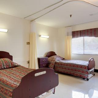 A well-lit hospital room featuring two beds with patterned bedding, designed for patient comfort.