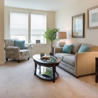 A cozy living room with a comfortable sofa and armchair, decorated with soft cushions and complemented by a central coffee table and lamp.