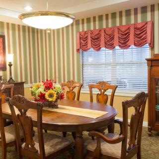 A cozy dining room featuring a wooden table with floral centerpiece, surrounded by matching chairs, set against striped wallpaper and illuminated by a chandelier.