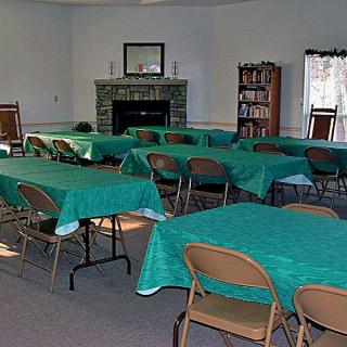A well-arranged event space with tables covered in green cloths, surrounded by chairs, and featuring a fireplace and bookshelf.