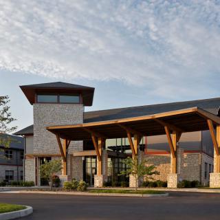 A modern building with prominent wooden beams and large windows, featuring an inviting entrance.